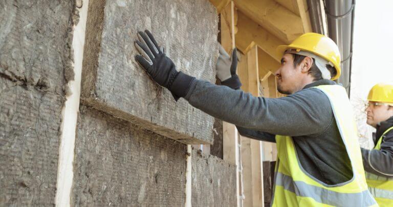 Construction workers placing eco insulation blocks on outer wall of house